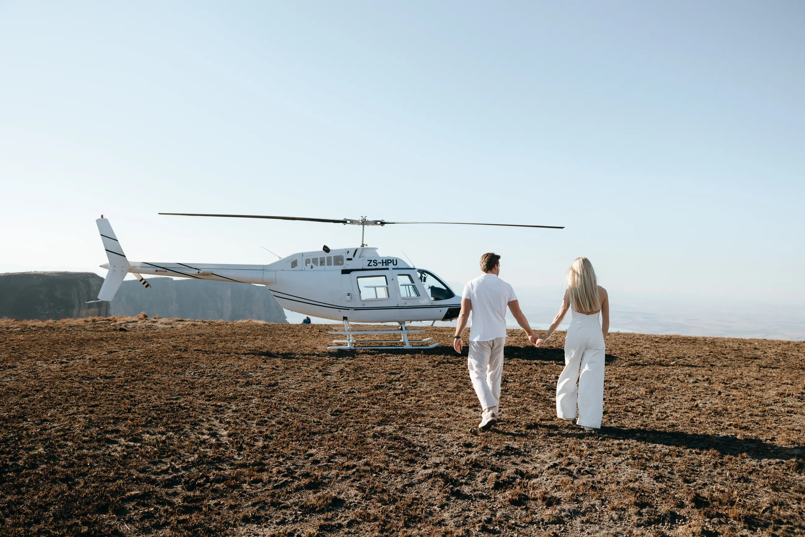 Christy and Joshua walking hand in hand across the plateau towards the waiting helicopter