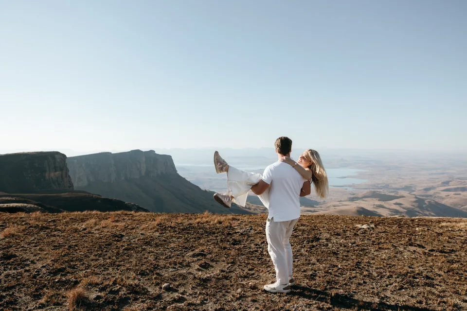 Christy and Joshua embracing on the escarpment edge with mountains behind them