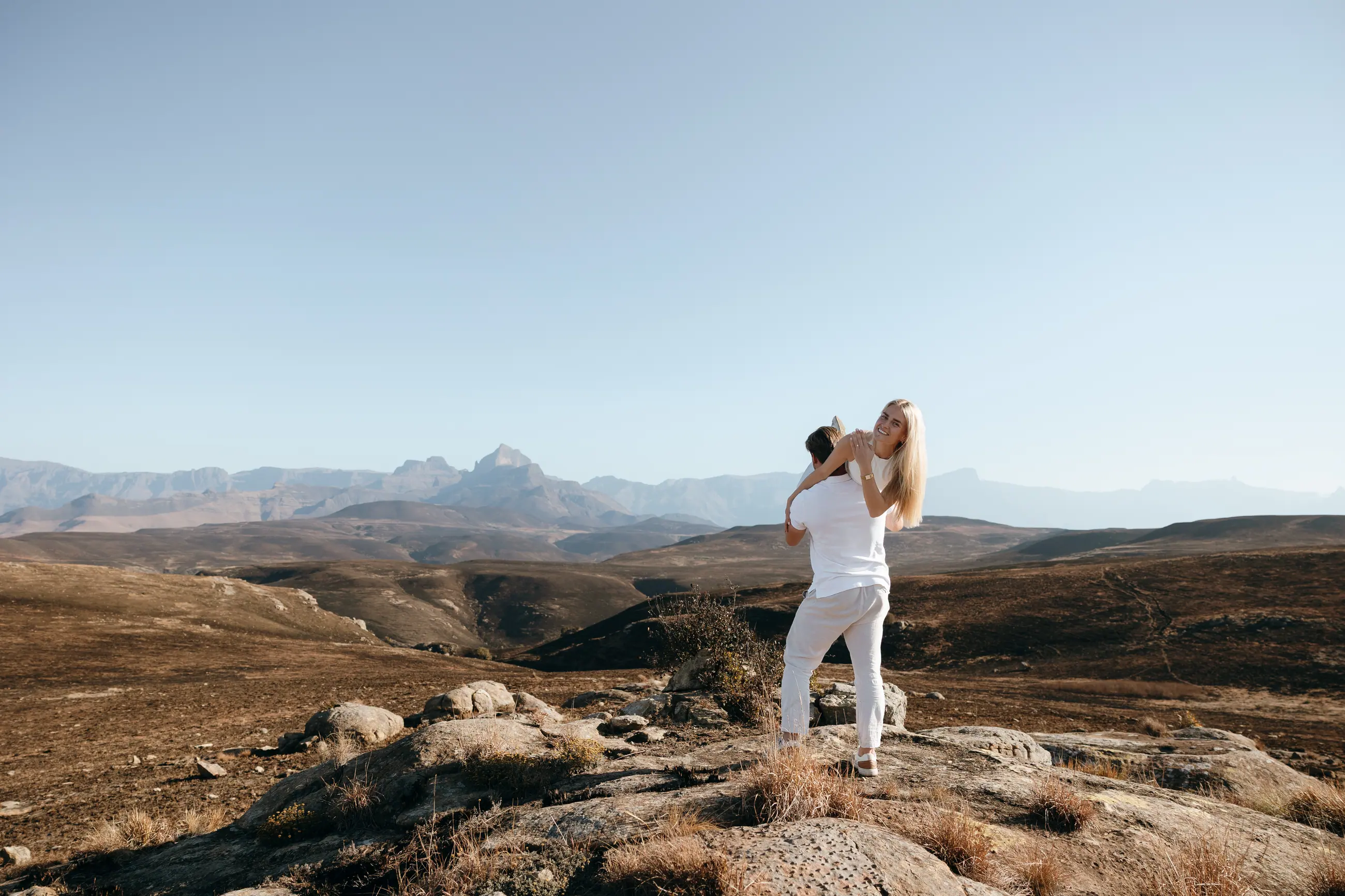 Joshua lifting Christy on a rocky outcrop, the Drakensberg stretching away behind them