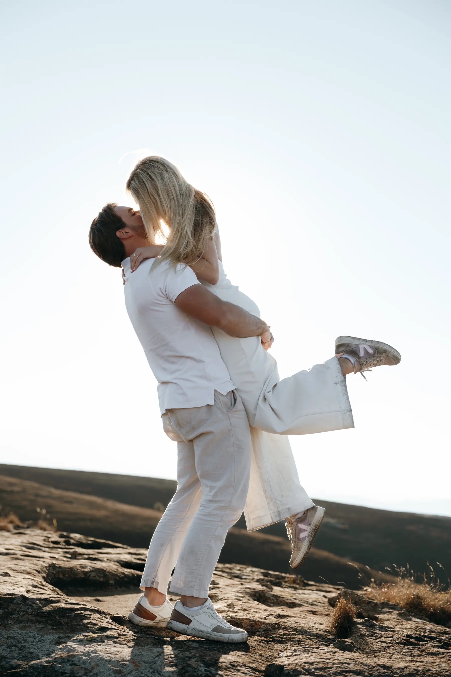Joshua lifting Christy in his arms on a rocky outcrop at golden hour
